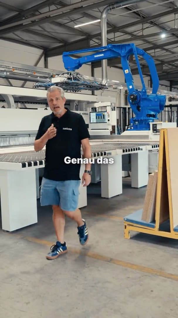 Schreiner geht durch die Produktionshalle der Fabrikatur an einem Roboterarm vorbei