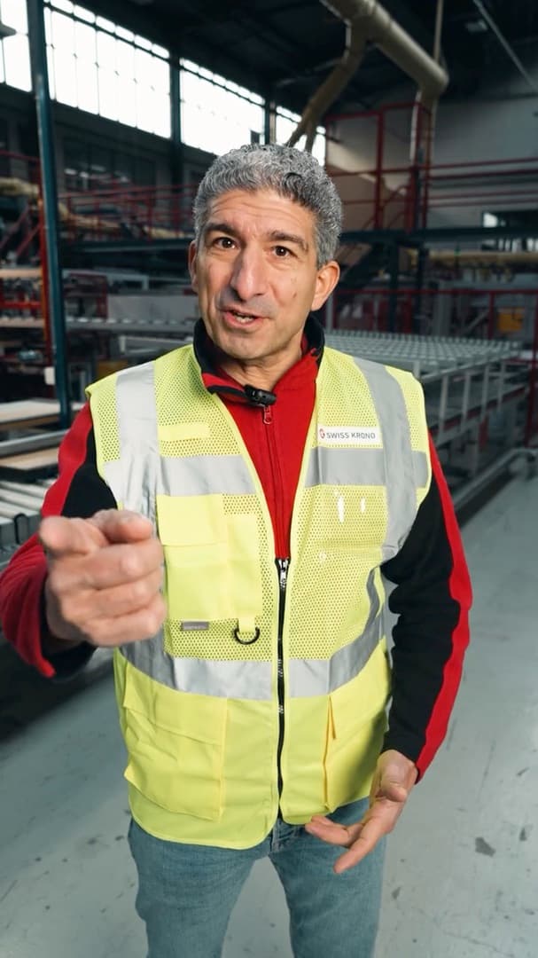 Mitarbeiter in Warnweste zeigt in einer Lagerhalle von Swiss Krono in die Kamera